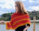 Chica con un pañuelo triangular crochet rojo y amarillo, apoyada en una barandilla de madera junto a un lago.