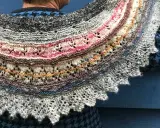 Un chal de lana tejido con hilos de colores, con un intrincado diseño de encaje y bordes festoneados. Los mantoncillos de crochet son una obra de arte.