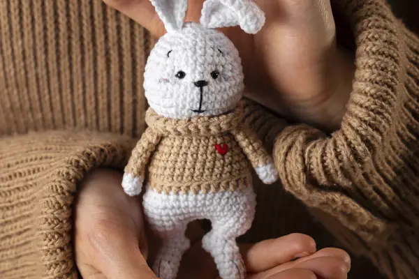 Un tierno conejito blanco con suéter tejido, parte de una colección de amigurumis originales, sostenido entre manos.
