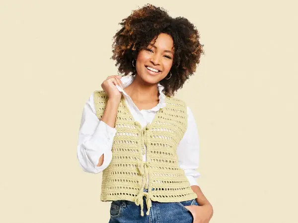 Mujer sonriente con chaleco de crochet con patrón calado, atado al frente.