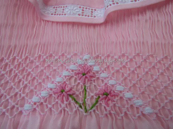 Detalle de puntada smock en tela rosa, con flores bordadas. Aprende como hacer punto smock.
