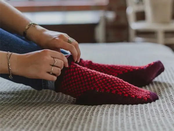 Manos ajustando calcetines rojos y morados tejidos a mano con agujas circulares.