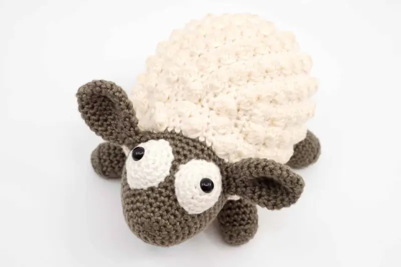 Oveja amigurumi de ganchillo con lana crema y marrón, ojos grandes y expresivos, lista para abrazar.